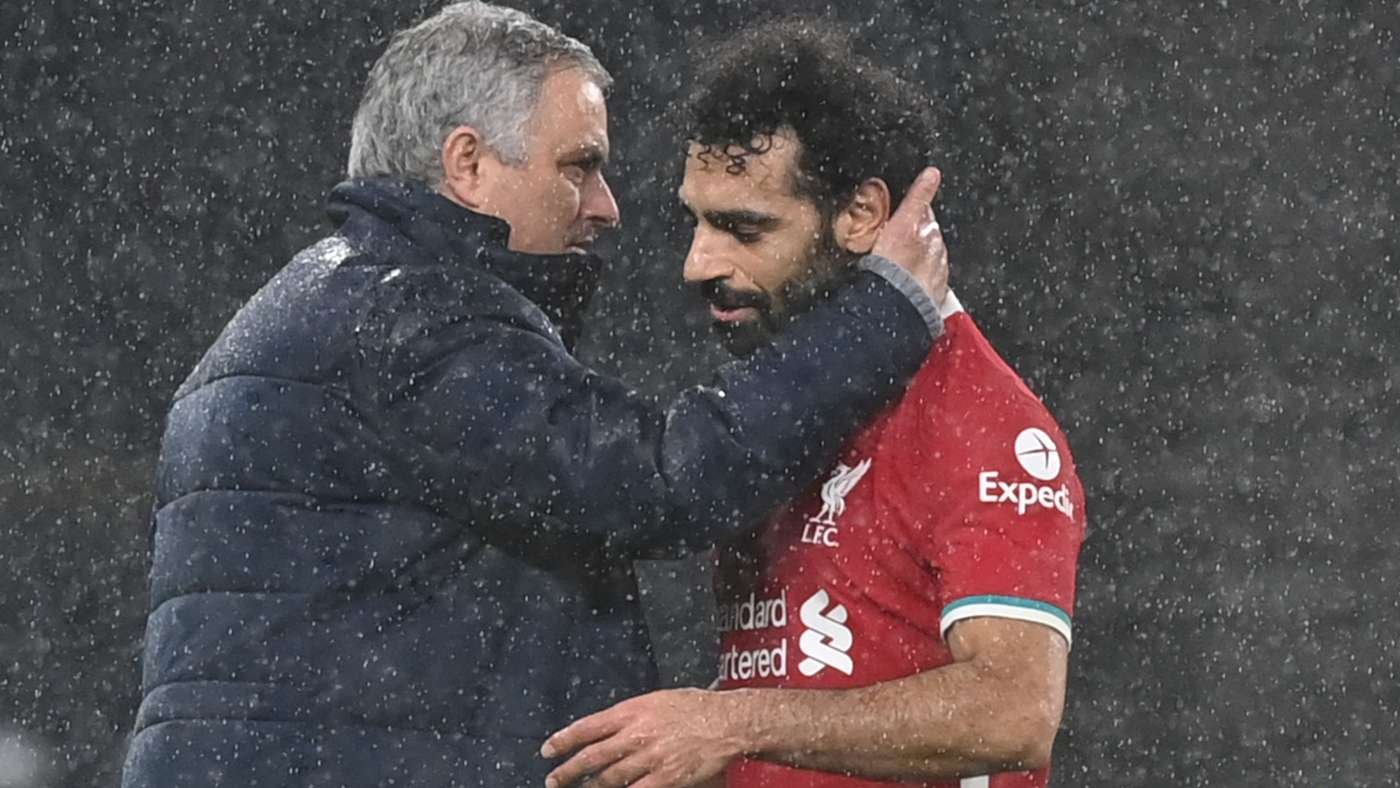 Two men embrace in falling snow; one in a red Liverpool FC jersey being consoled by a coach in a dark jacket.