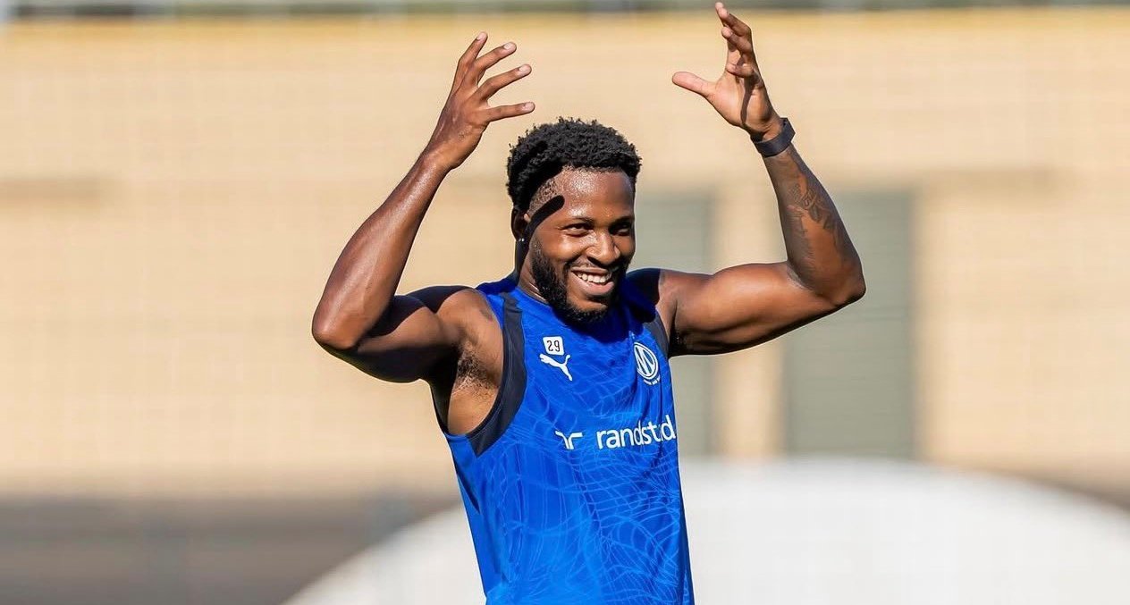 Athlete in a blue training jersey raises his arms in celebration on a sunny field.” (informative)