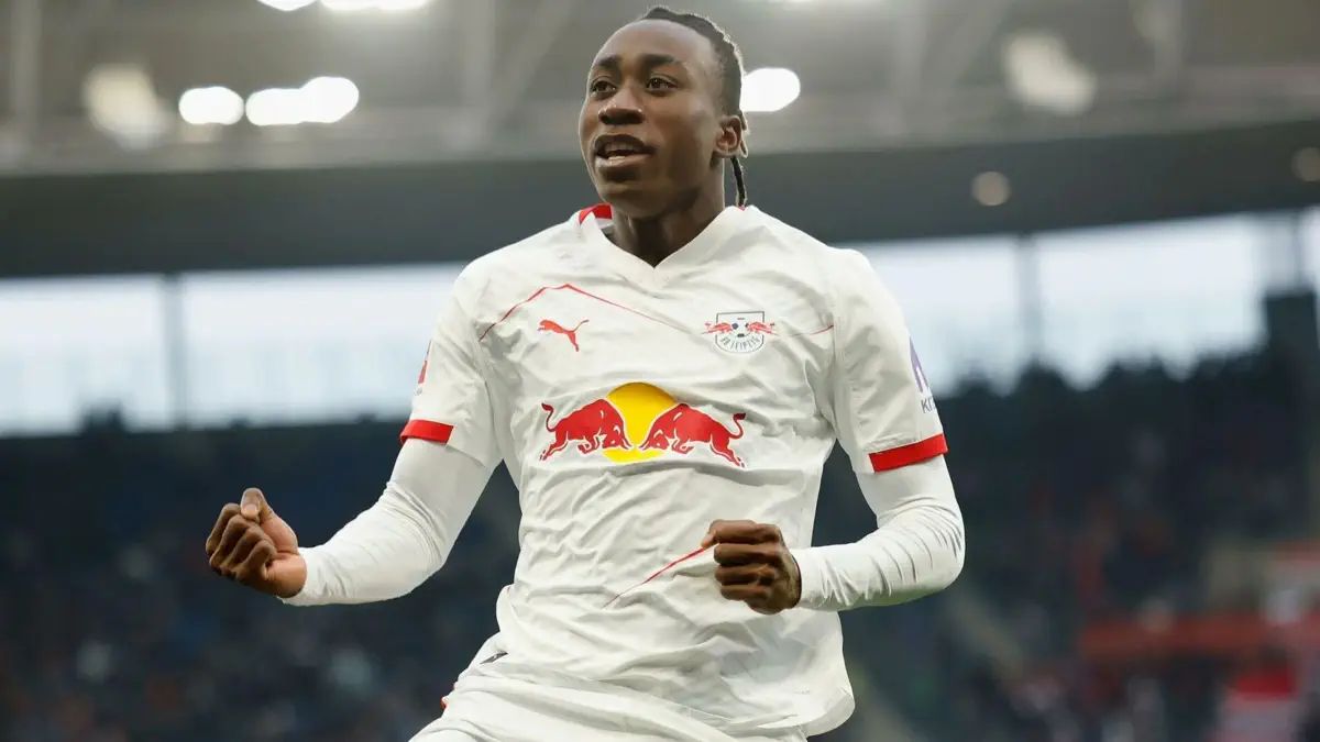 Soccer player in a white kit with Red Bull logo celebrates on the field, arms raised in joy amid a stadium crowd.