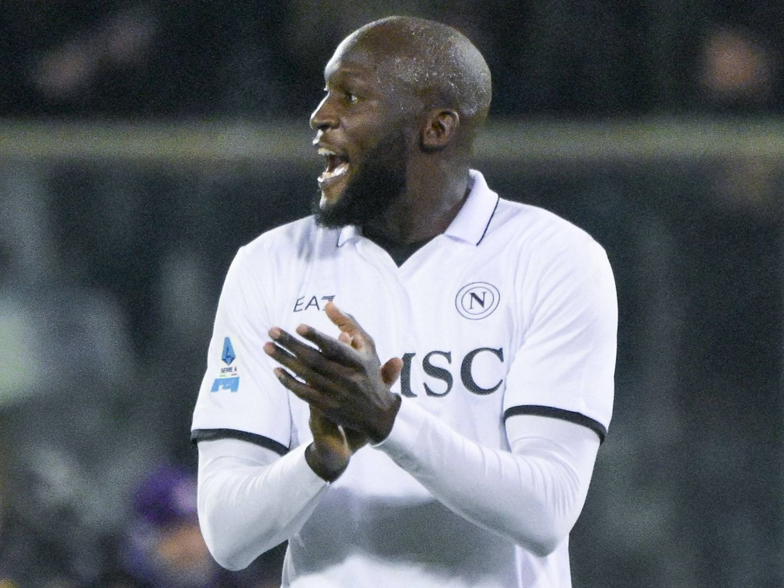 Black male soccer player in a white jersey clapping on the field at night, celebrating a moment during a match.