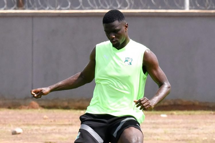 Soccer player in a neon green training vest performing a drill on a dusty outdoor field.