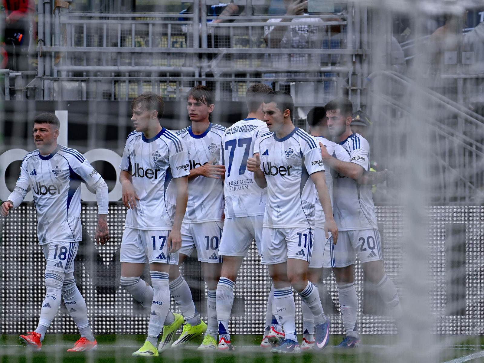 Soccer players in white Uber jerseys walk together on the field after a match, with a hazy barrier in the foreground.