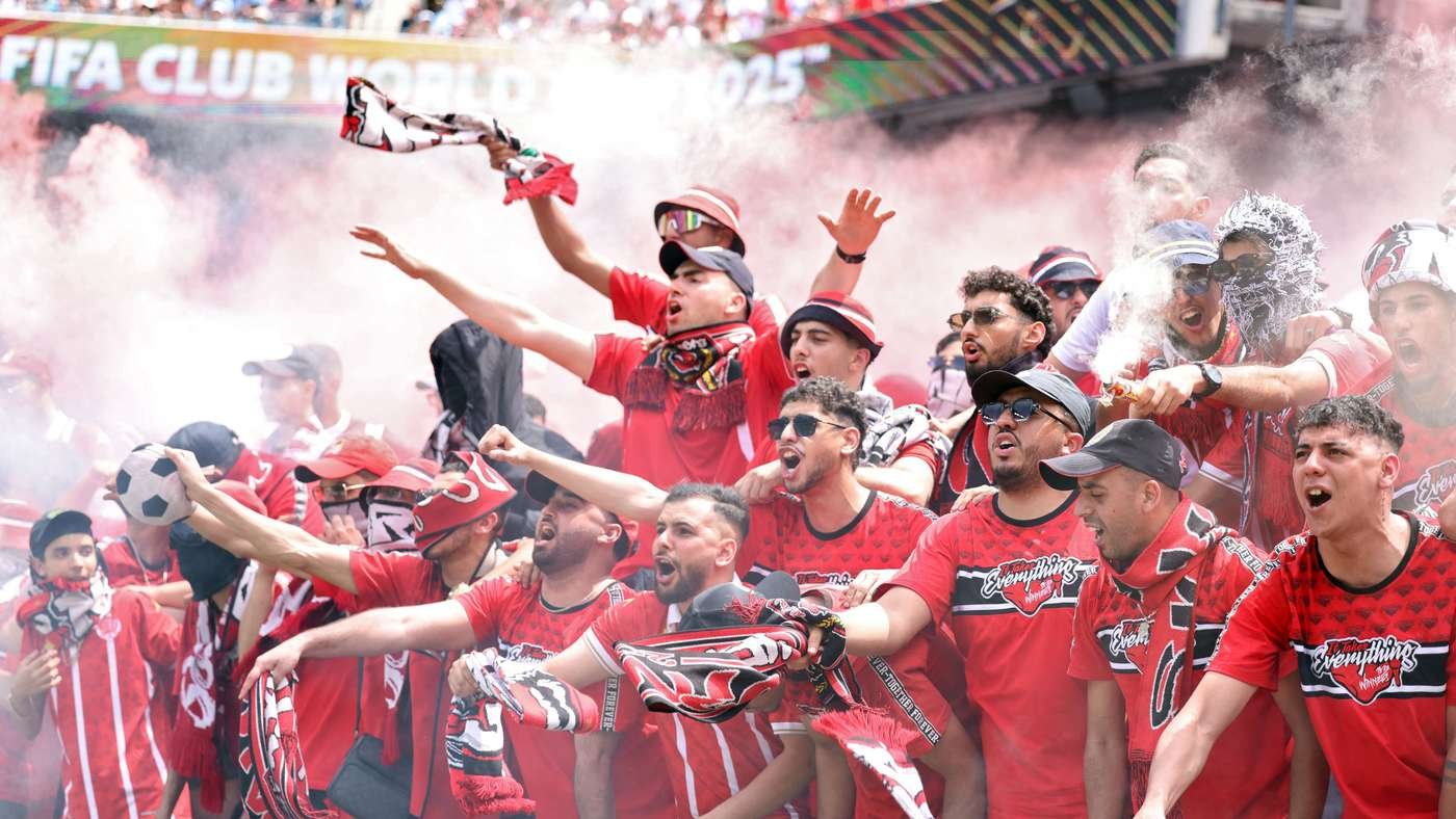 Crowd of red-clad soccer fans celebrating with scarves and smoke at a stadium, cheering for their team during a FIFA event (2015).
