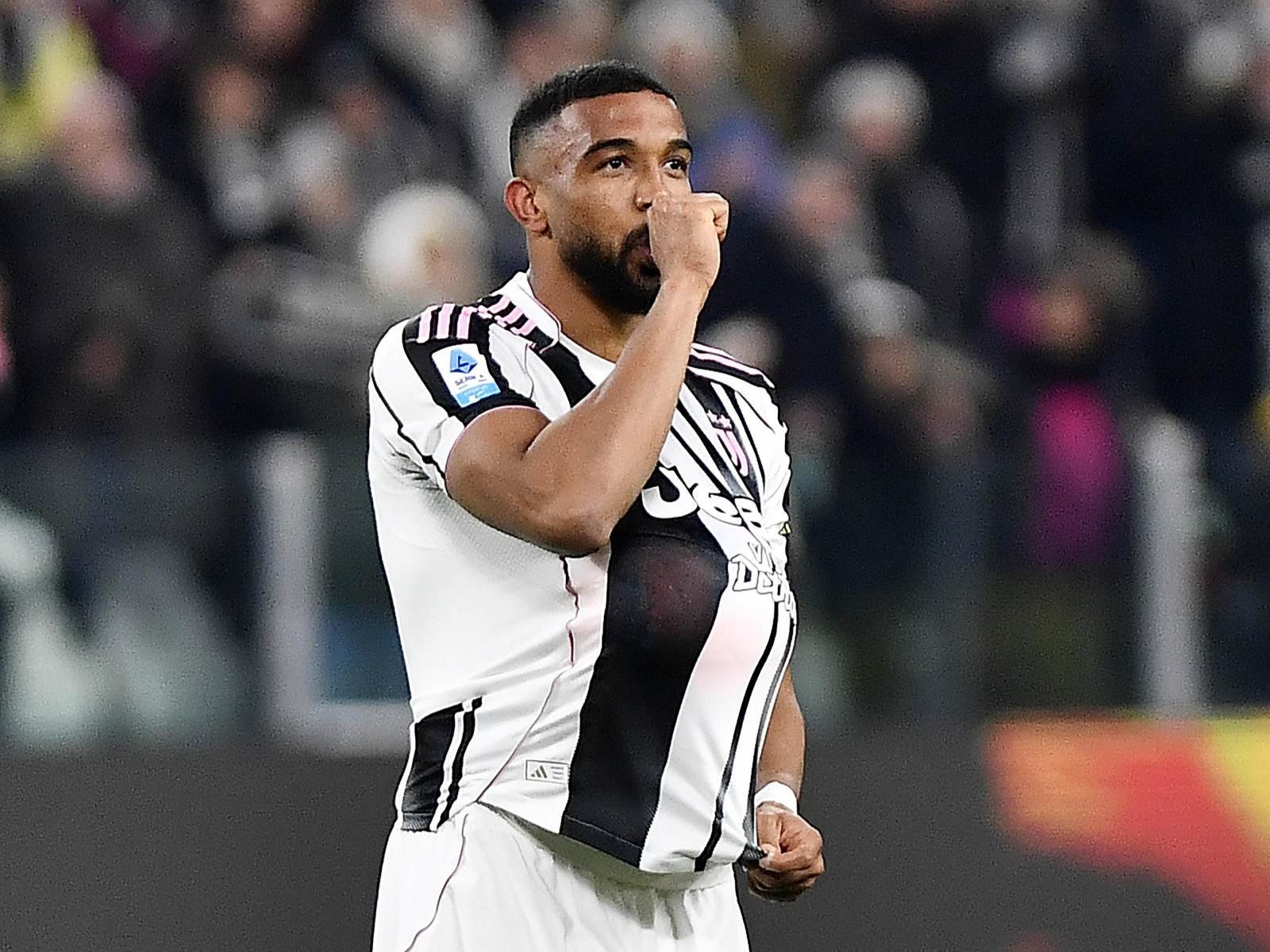 Juventus soccer player in a white and black striped kit celebrating with a fist near his mouth on the field