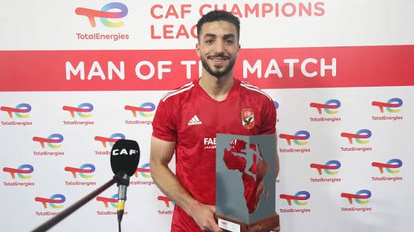 Male footballer in a red jersey holding a trophy, standing in front of a backdrop that reads 'MAN OF THE MATCH' with CAF Champions League and TotalEnergies logos.