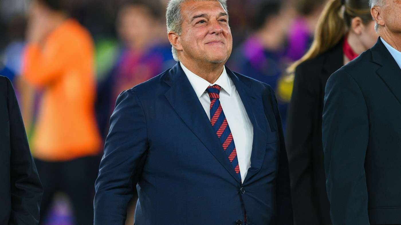 Smiling man in a navy suit and red striped tie at a formal outdoor event, surrounded by people in the background