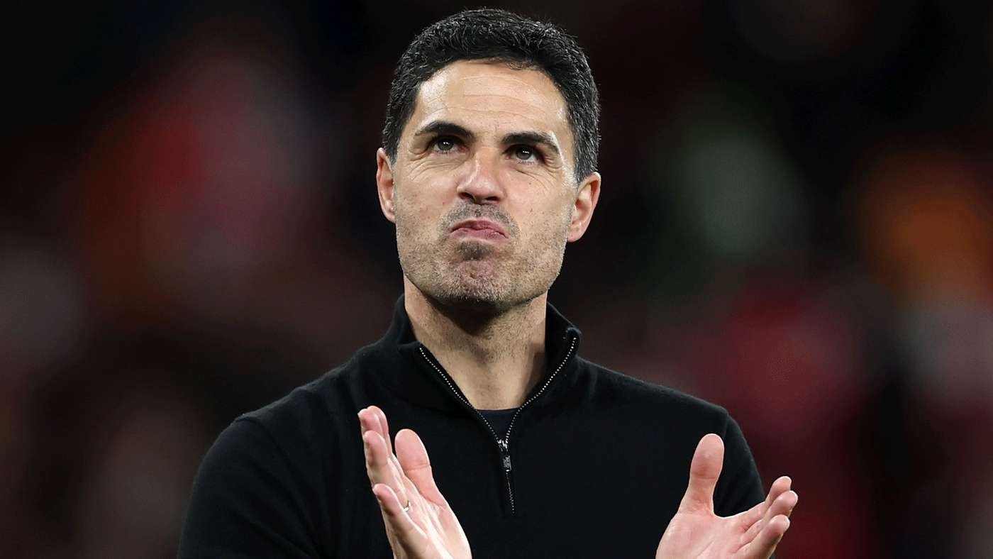 Man in a black zip sweater applauding on a blurred stadium background.
