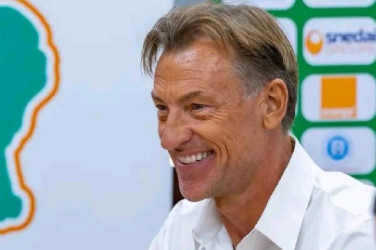 Smiling man in a white shirt at a press event, with sponsor logos in the background.