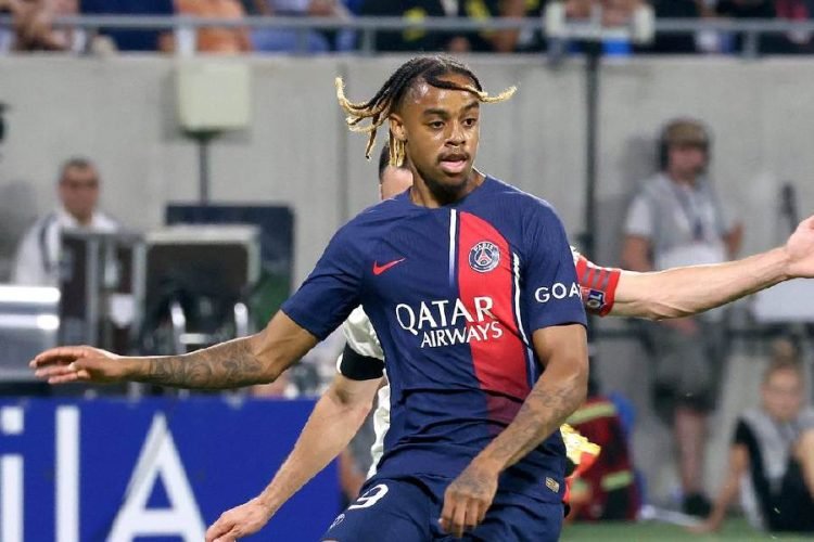 PSG footballer in a navy kit with a red stripe and Qatar Airways logo, extending his arms during a soccer match.