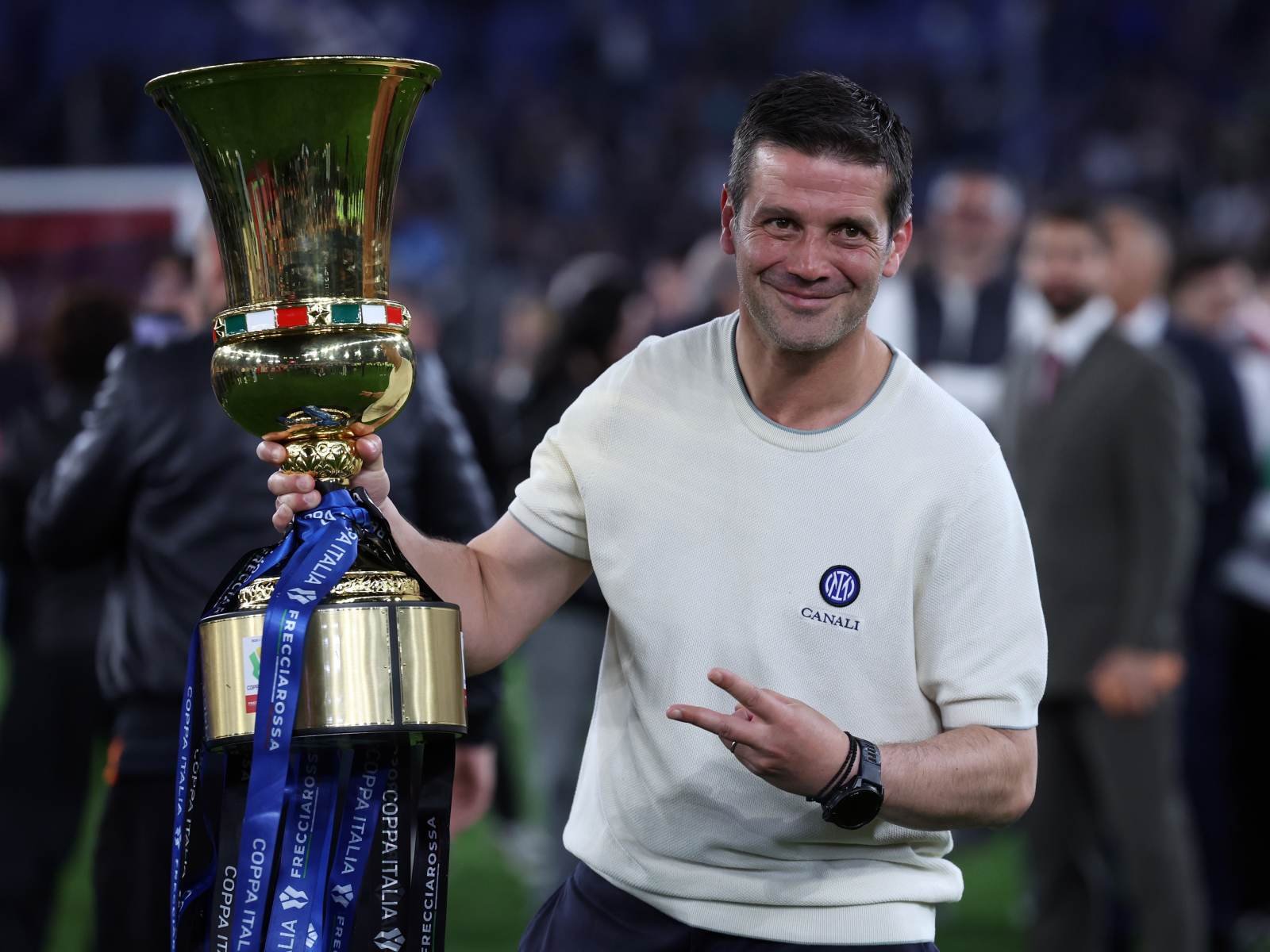 Man in a light sweater holding a large gold trophy with Italian flag colors, smiling at a trophy presentation.','Athlete celebrates winning, posing with a tall gold cup and blue ribbons at a sports event.','Smiling man wearing a white Canali sweatshirt holds a tall gold trophy with blue ribbons.','Portrait of a sports winner holding a grand trophy during a ceremony, with a crowd in the background.','Trophy presentation: gold cup adorned with an Italian flag band, blue ribbons, and a victorious gesture.