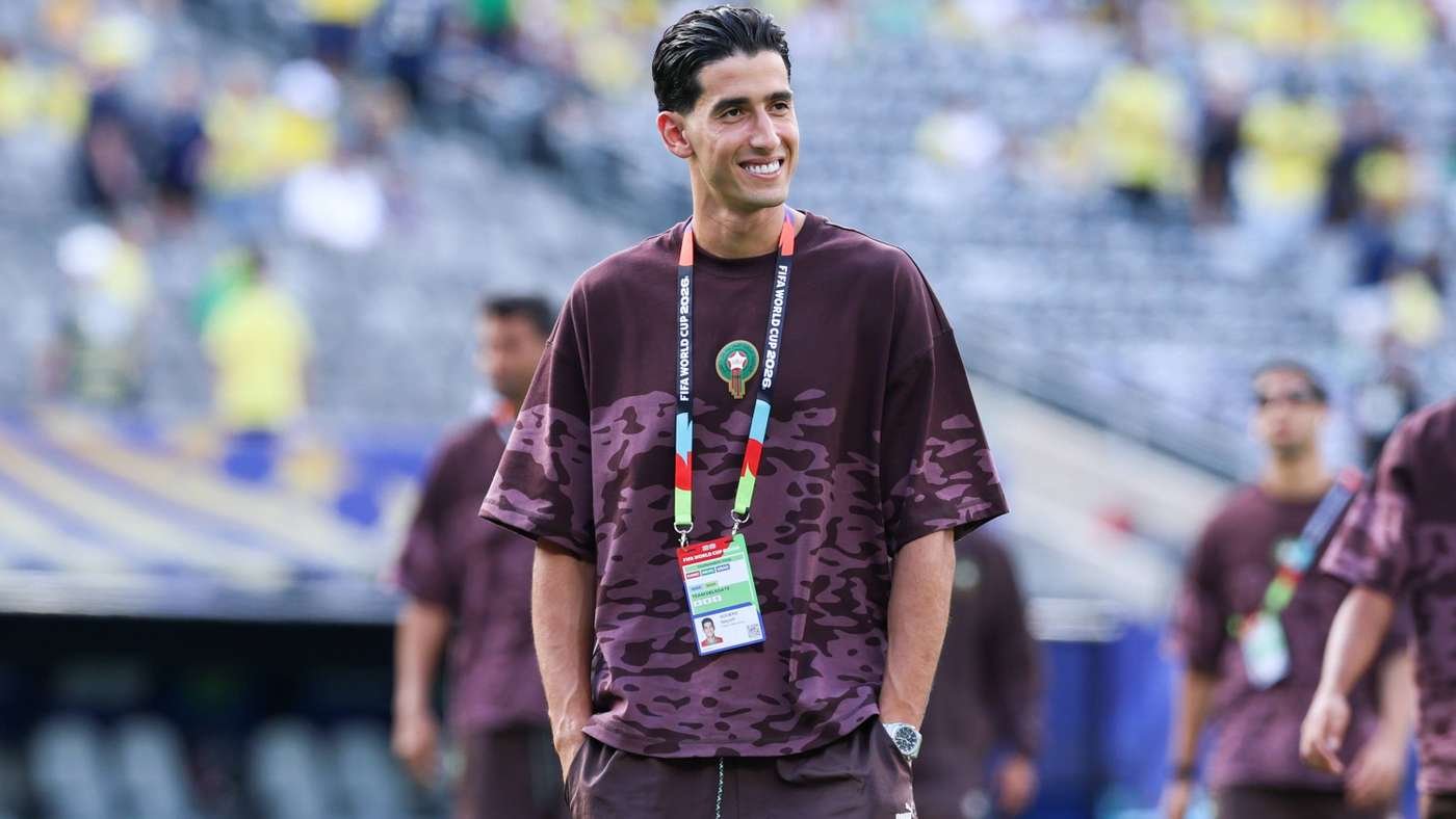 Man in maroon camouflage shirt with lanyard and ID badge at a stadium, smiling on the field.