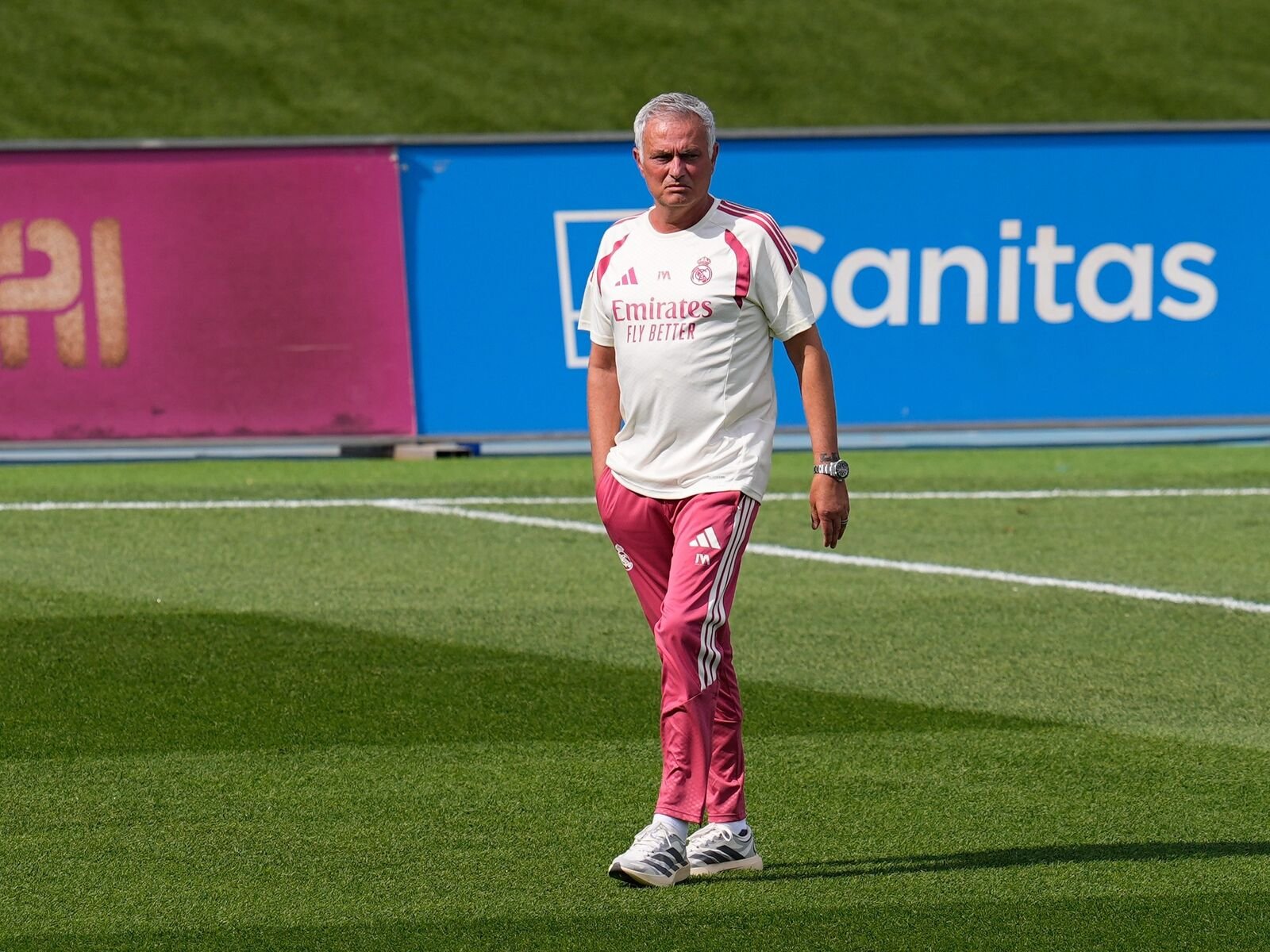 Man in white and pink Real Madrid training kit walking on a football pitch with a blue advertising board in the background (Emirates Fly Better).