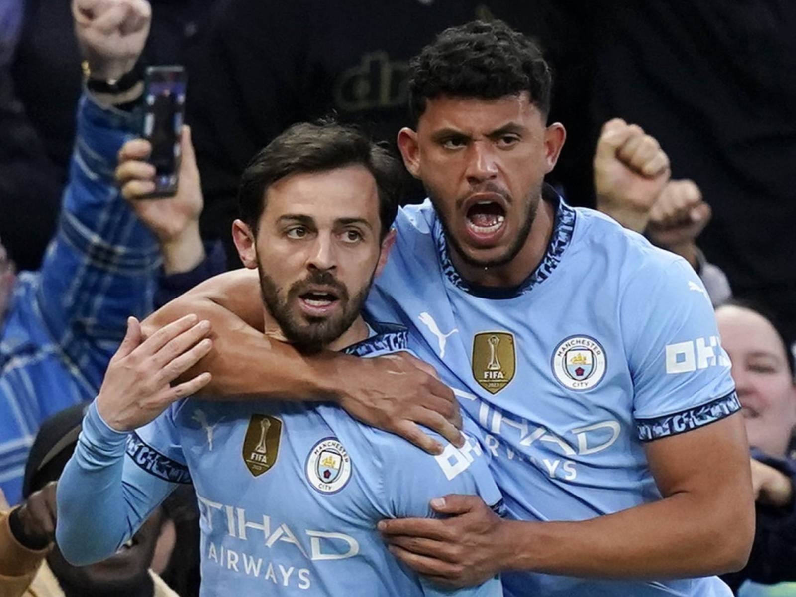 Manchester City players celebrate a goal, embracing each other in light blue uniforms.