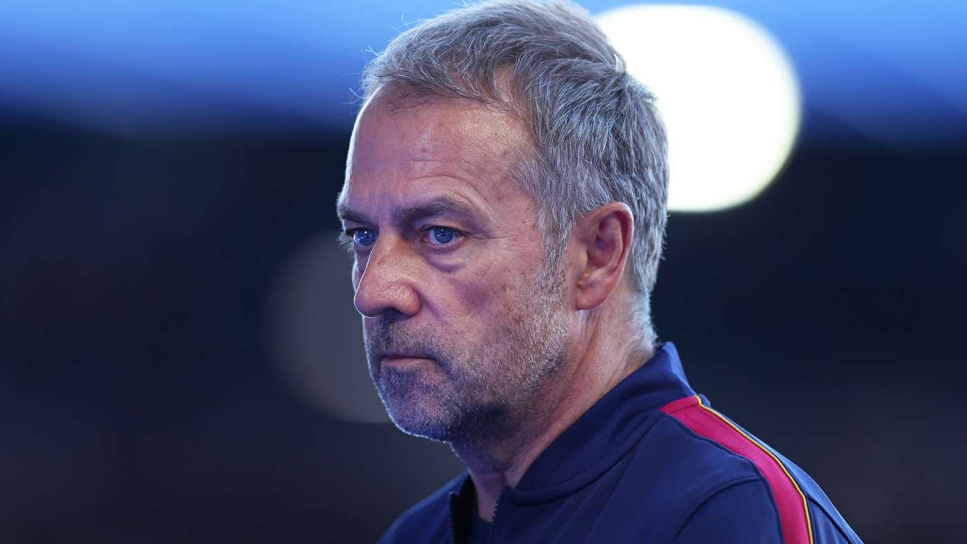Side profile of a middle-aged man with gray hair and stubble, wearing a blue athletic jacket with red and yellow stripes, looking serious.