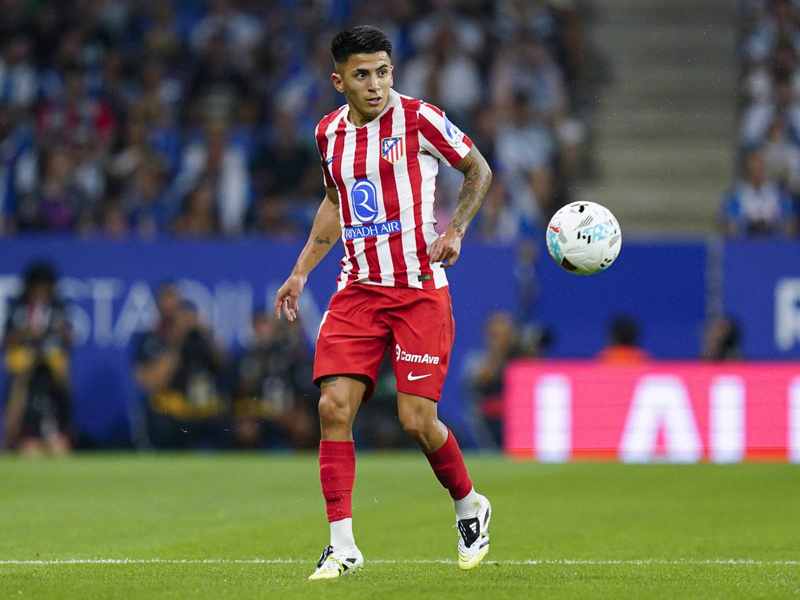 Soccer player in a red-and-white striped Atlético Madrid kit controls the ball on the field during a match.