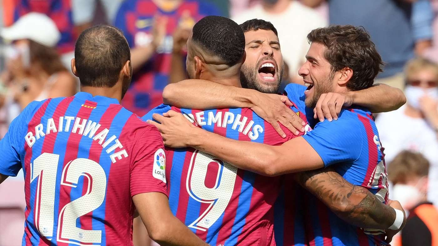 Group of FC Barcelona players celebrating a goal with arms around each other on the field.