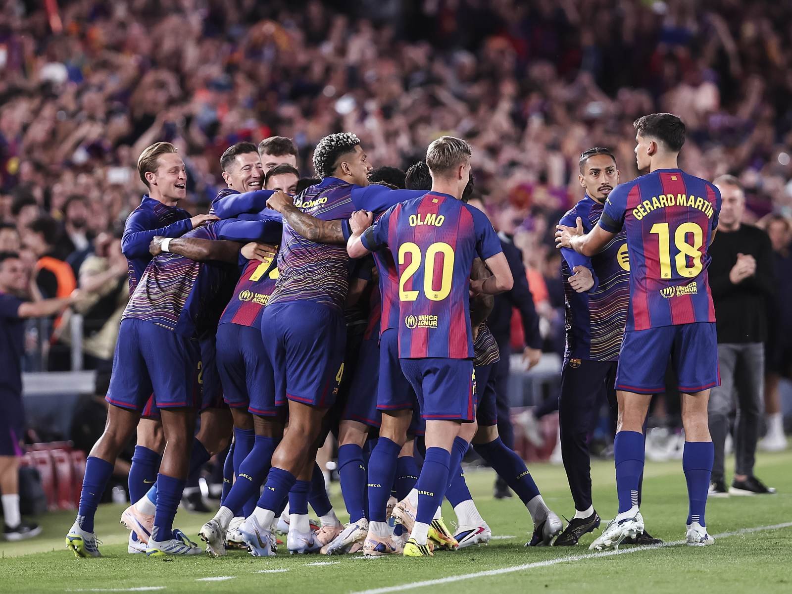 Soccer players in blue-red uniforms celebrate in a group hug on the field as the crowd cheers in the stands behind them. Soccer players in blue-red uniforms celebrate in a group hug on the field as the crowd cheers in the stands behind them.