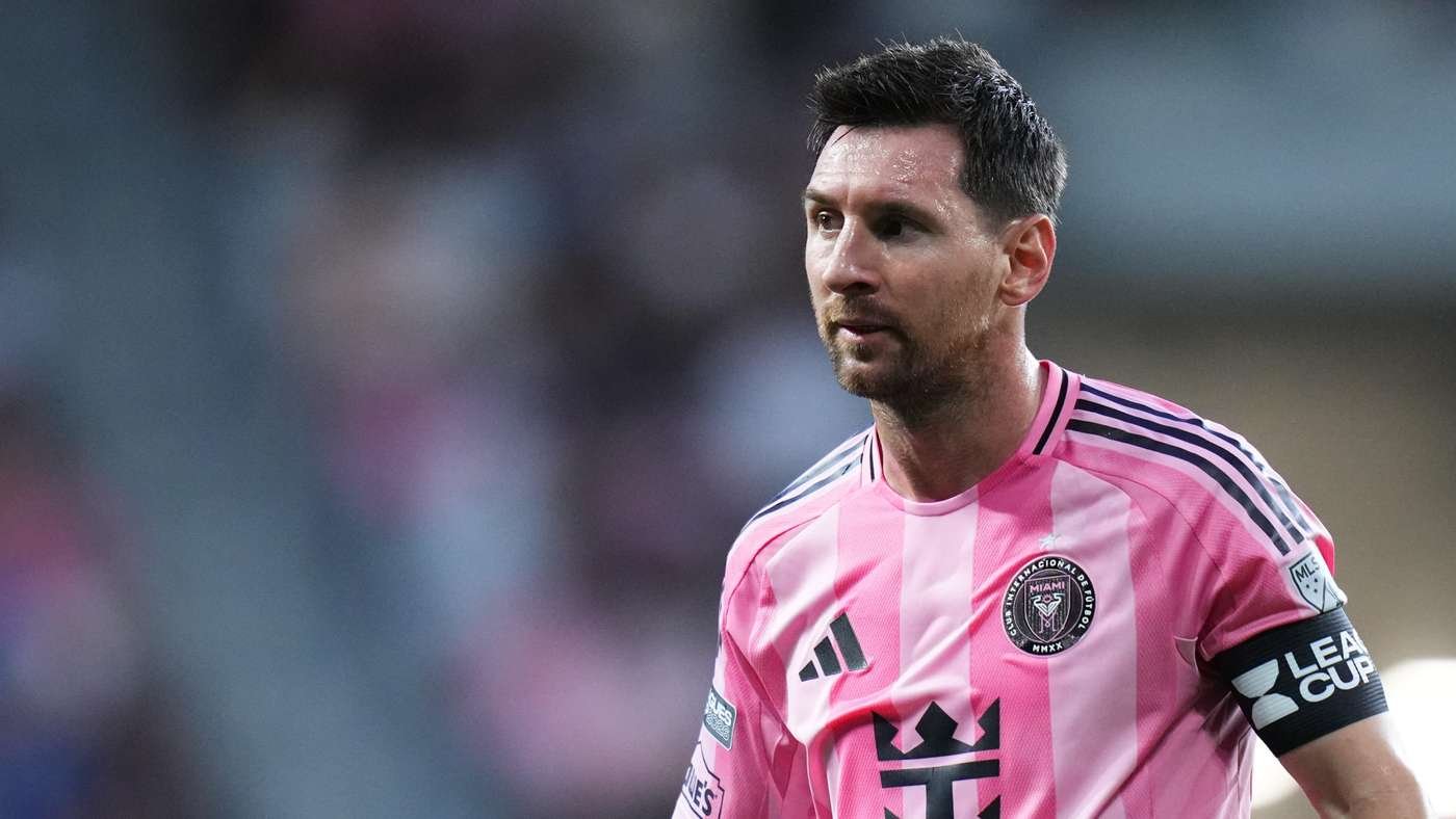 Professional soccer player in a pink striped jersey with a team crest, looking intently to the right during a match.