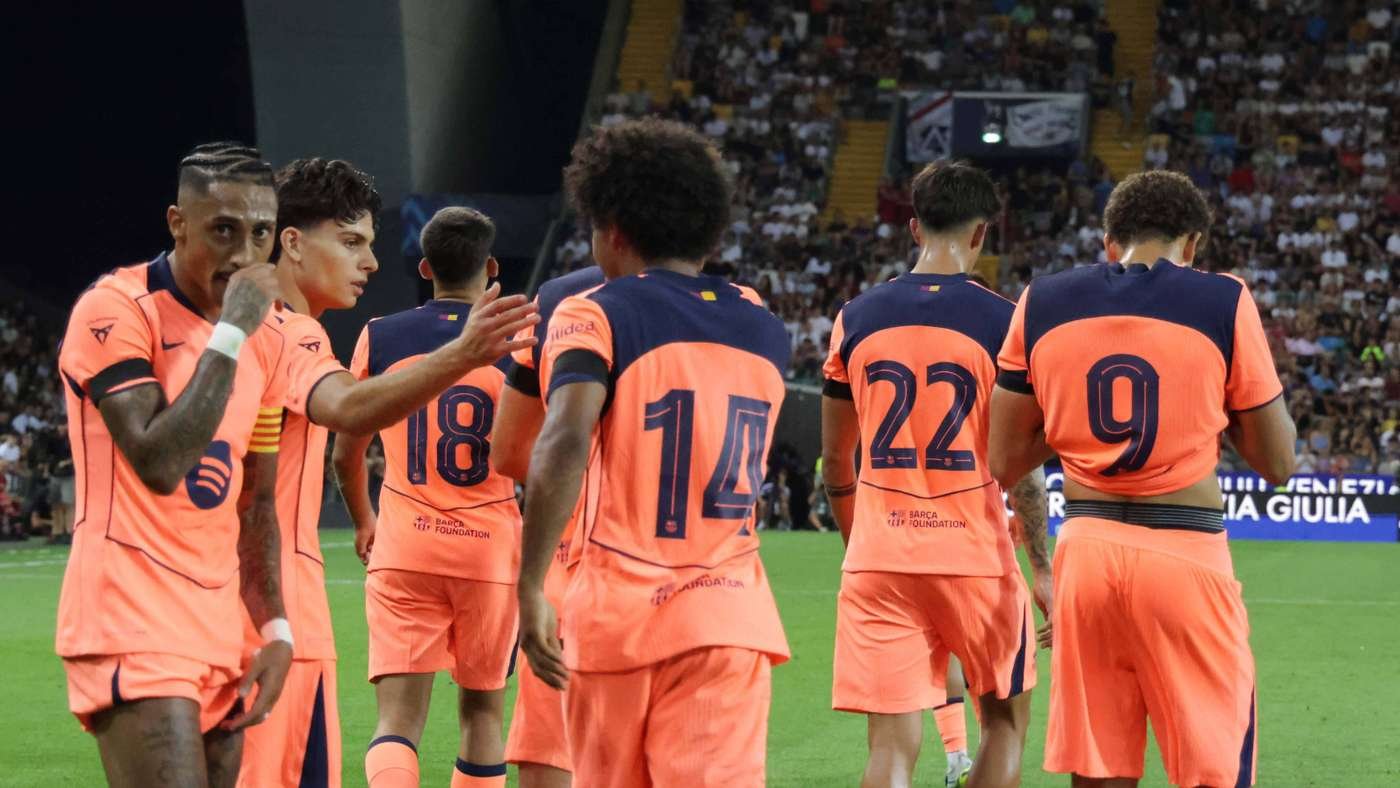 Soccer players in bright orange kits stand on the field with a cheering crowd in the stands behind them, backs to the camera.