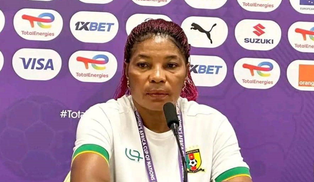 Female athlete speaks at a press conference, seated in front of a purple sponsor backdrop with logos.