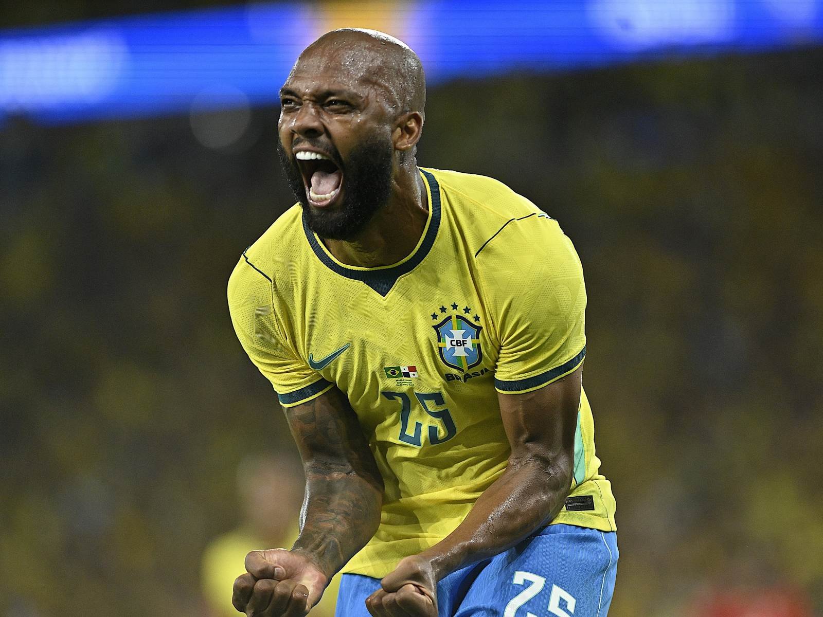 Brazilian soccer player in a yellow Brazil kit shouting with fists clenched in celebration on the field