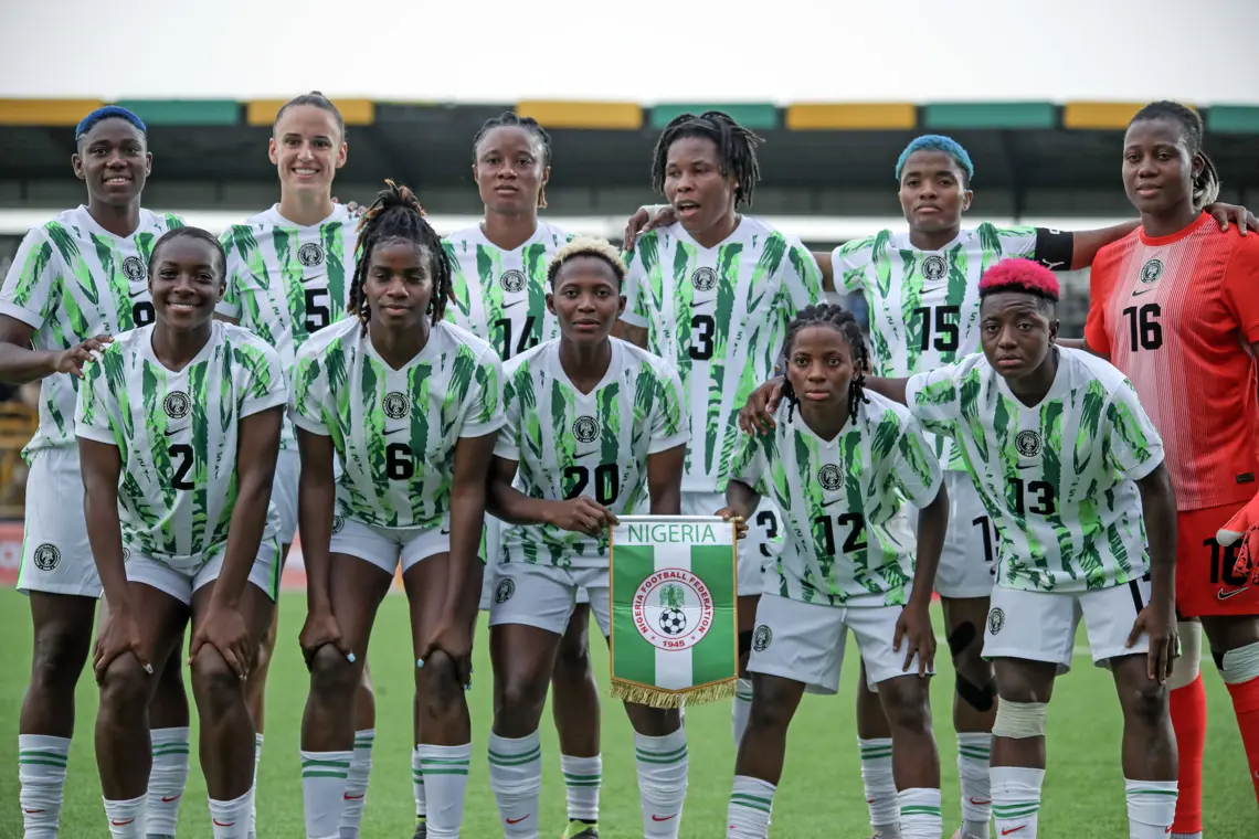 Nigeria women's football team posing for a group photo in green-and-white kits with the federation banner reading 'NIGERIA' in front.