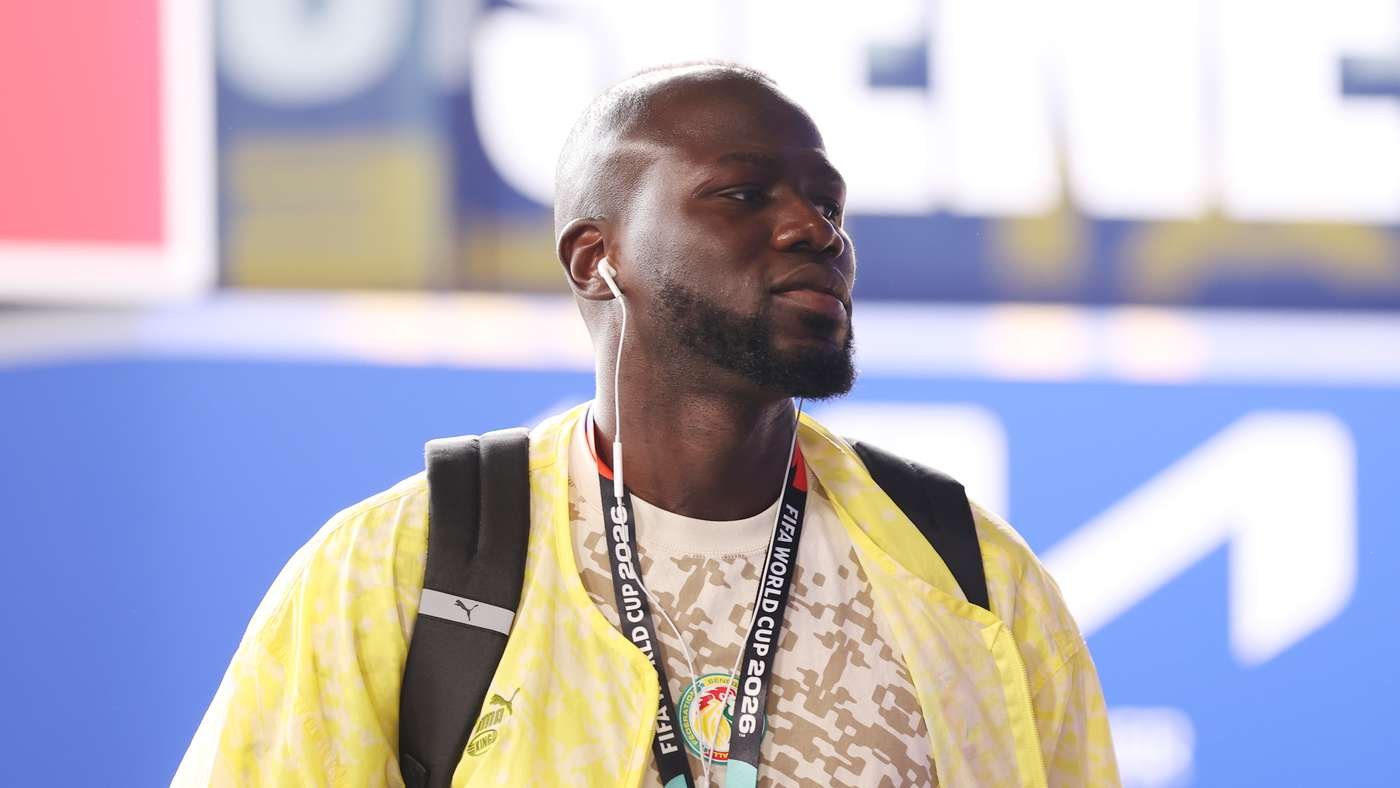 Man with a backpack and a yellow jacket wearing white earbuds, standing at a sports venue.