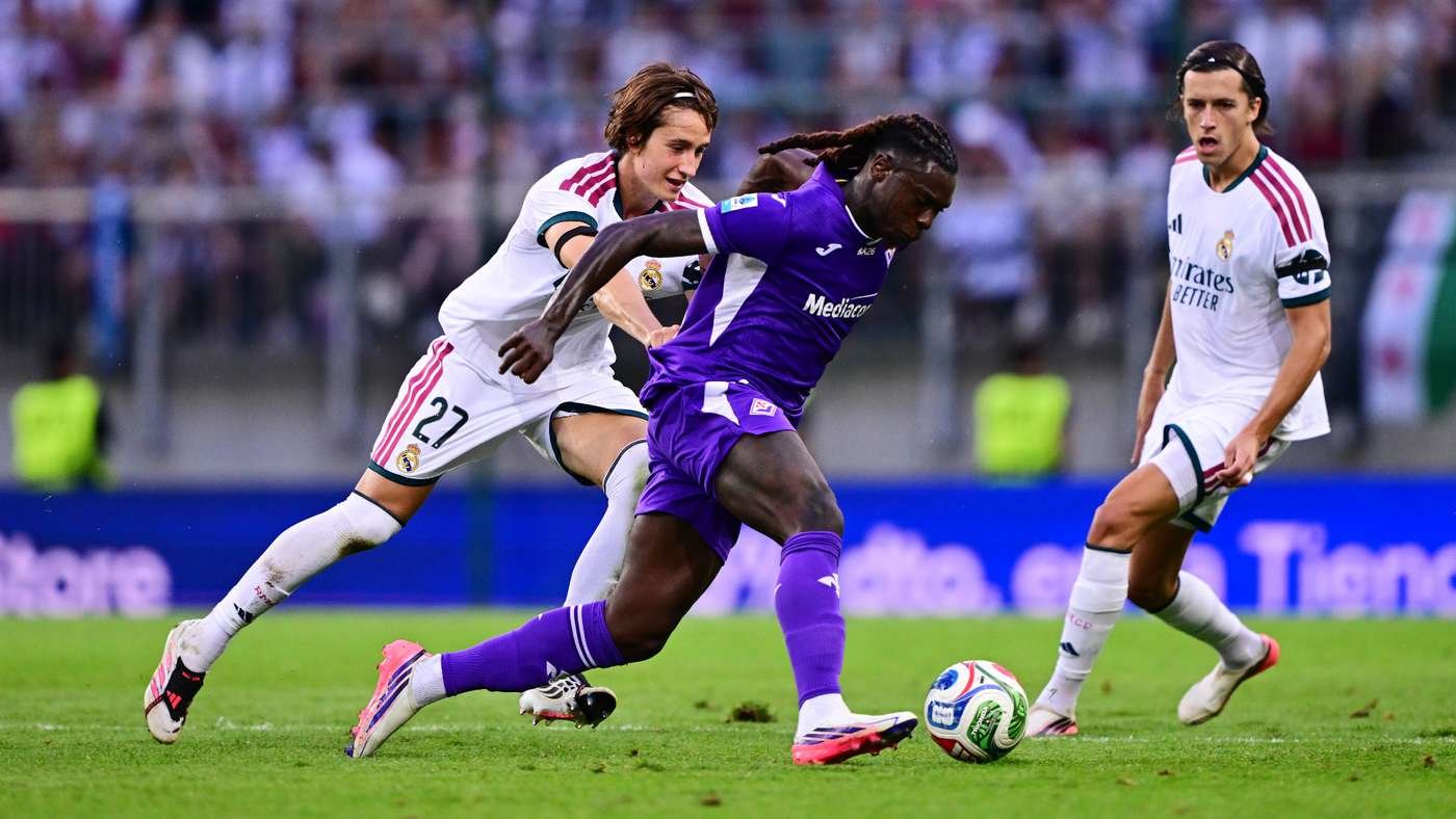 Soccer players compete for the ball during a match: a purple-clad player dribbles while two Real Madrid players in white jerseys close in from opposite sides on a green pitch. Soccer players compete for the ball during a match: a purple-clad player dribbles while two Real Madrid players in white jerseys close in from opposite sides on a green pitch.