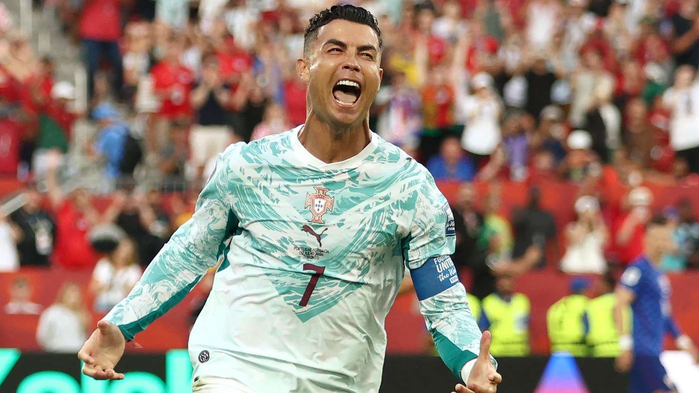 Soccer player in Portugal kit celebrates with mouth open, crowd cheering in the stands behind him, captain's armband visible on his arm. Soccer player in Portugal kit celebrates with mouth open, crowd cheering in the stands behind him, captain's armband visible on his arm.