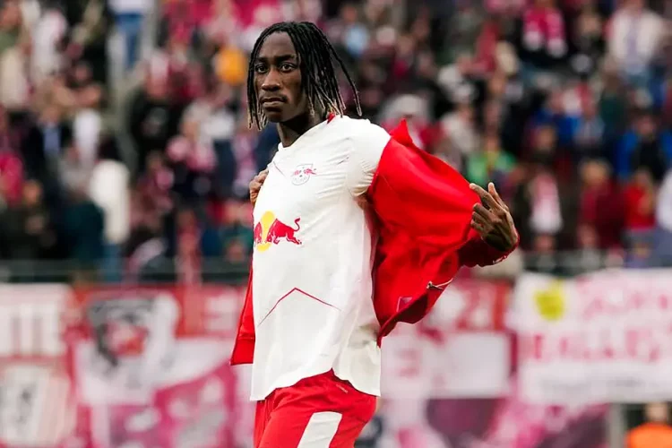 Soccer player on a field pulling off a white jersey with red sleeves and Red Bull logo, crowd cheering in the background.