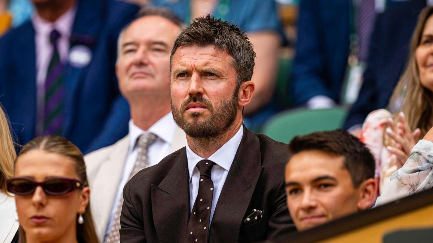 Man in a dark suit with a white shirt and polka-dot tie sits among spectators at a formal outdoor event, looking focused and serious. Man in a dark suit with a white shirt and polka-dot tie sits among spectators at a formal outdoor event, looking focused and serious.