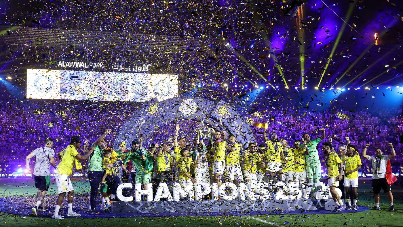 Football team in yellow celebrates on the field with a trophy, confetti raining down, and a large 'CHAMPIONS' sign in front.
