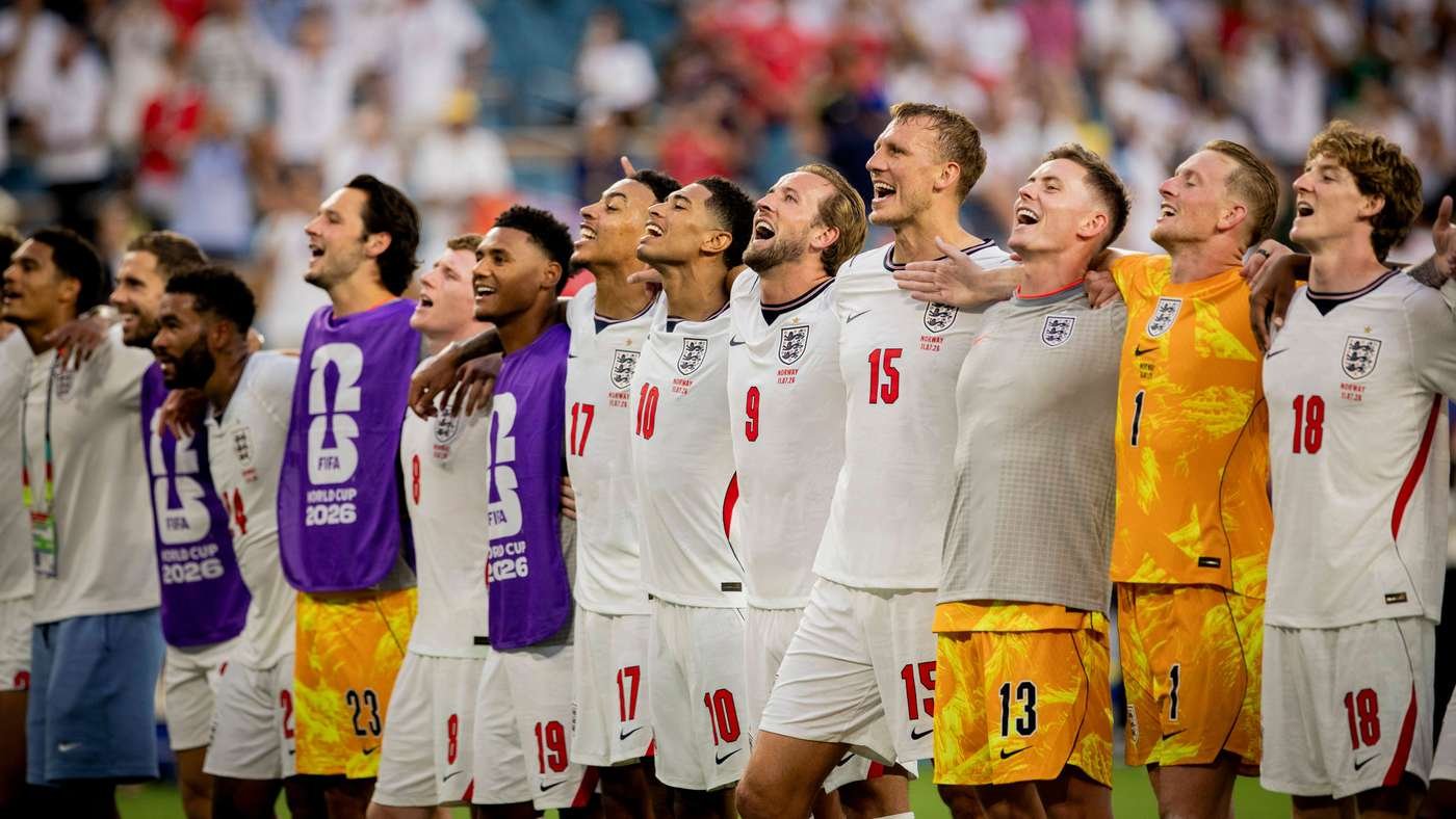 England football team players stand in a row with arms around each other, celebrating on the pitch.