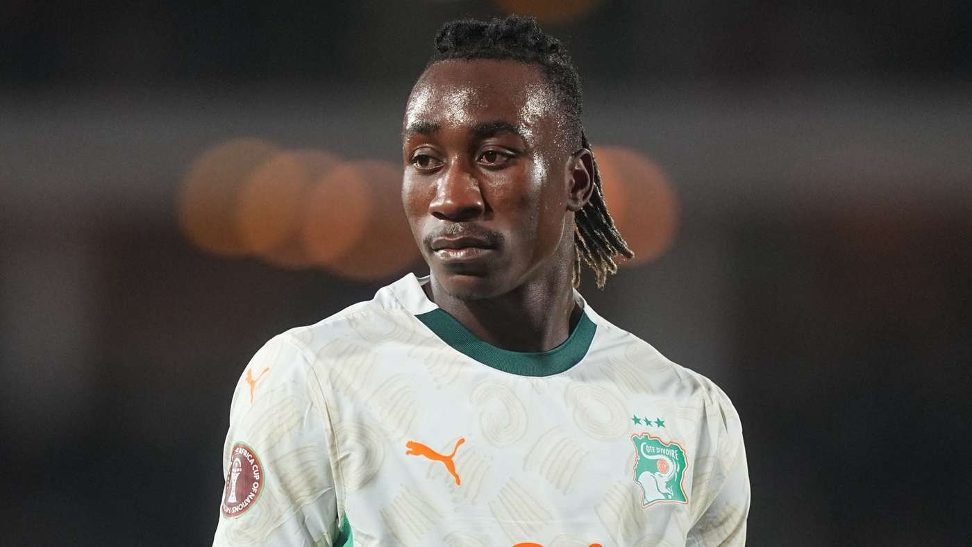 Close-up of a male soccer player in Ivory Coast kit, white jersey with green collar, looking to the left on the pitch.