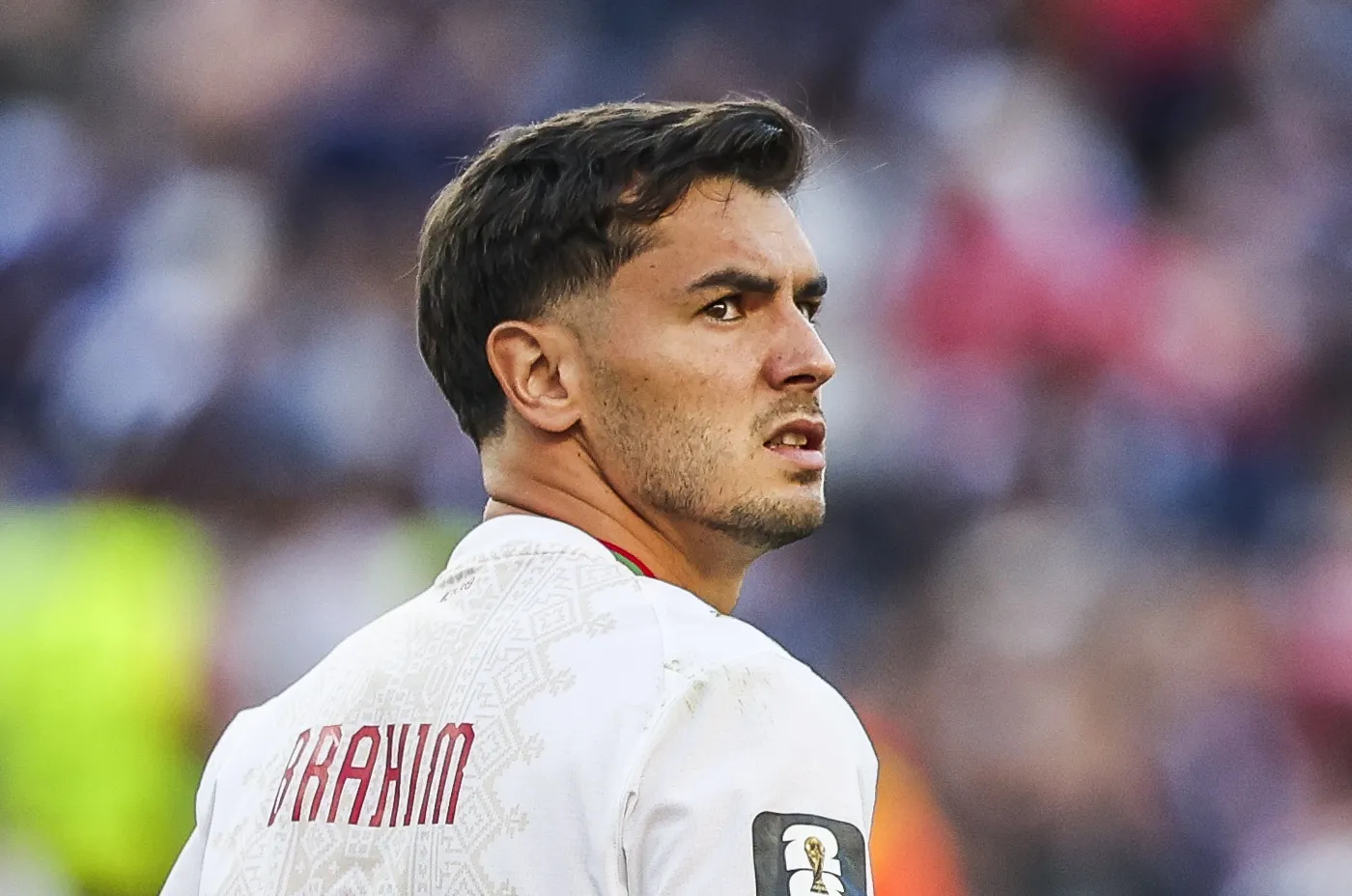 Soccer player in a white jersey seen from behind, with the name ABRAHAM on his back, looking over his shoulder during a game.