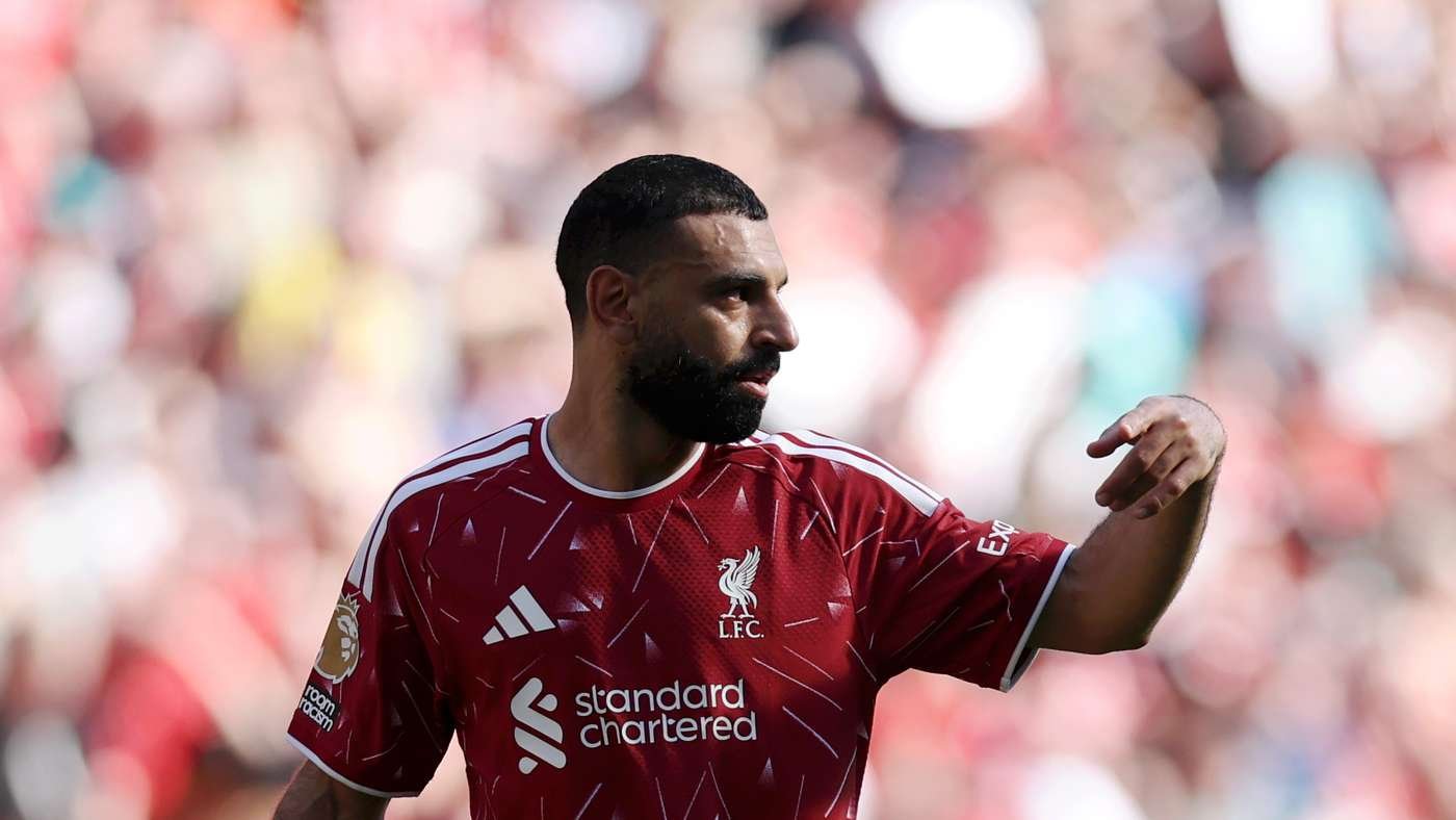 Mohamed Salah in a red Liverpool jersey on the field, looking to the right with his arm raised in a gesture.