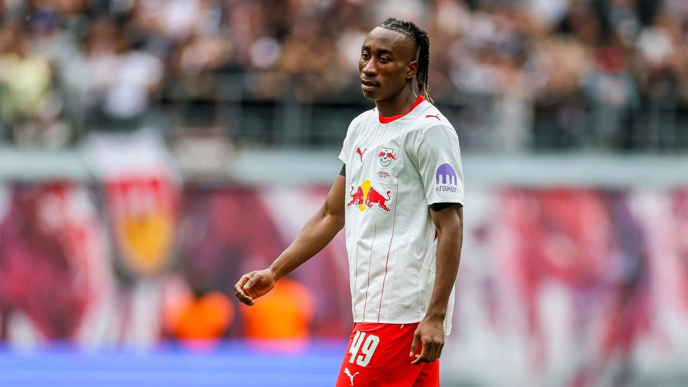 Soccer player in a white jersey with Red Bull logo and number 49 standing on a football pitch during a match. Crowds in the blurred background.