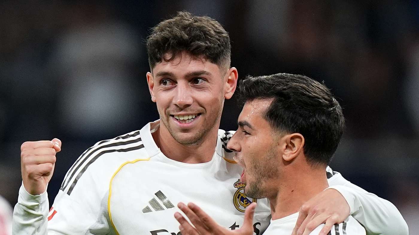 Two Real Madrid teammates celebrate together on the pitch, one with a clenched fist and the other smiling.