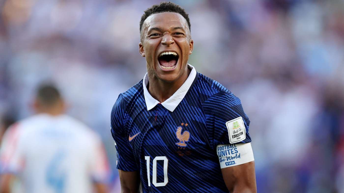 French footballer celebrating a goal, shouting with mouth wide open, wearing blue France kit with number 10 and a white armband on the sleeve.