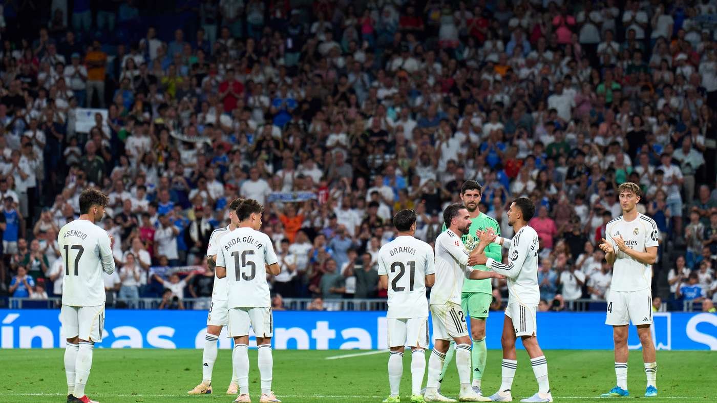 Real Madrid players in white celebrate on the pitch as fans cheer in the stadium behind them.