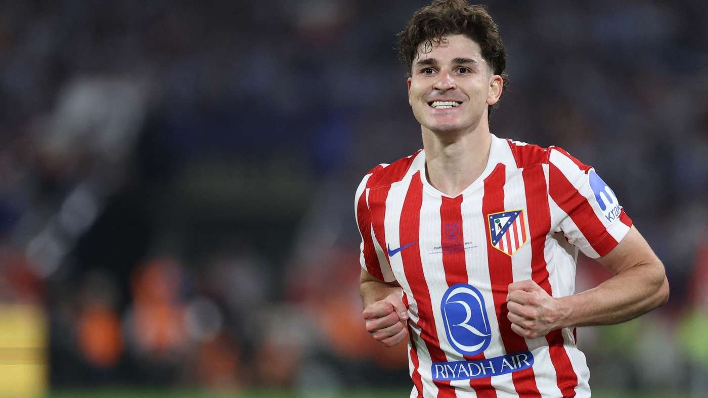 Atlético Madrid player in red-and-white striped jersey celebrates on the soccer field during a match, smiling."
