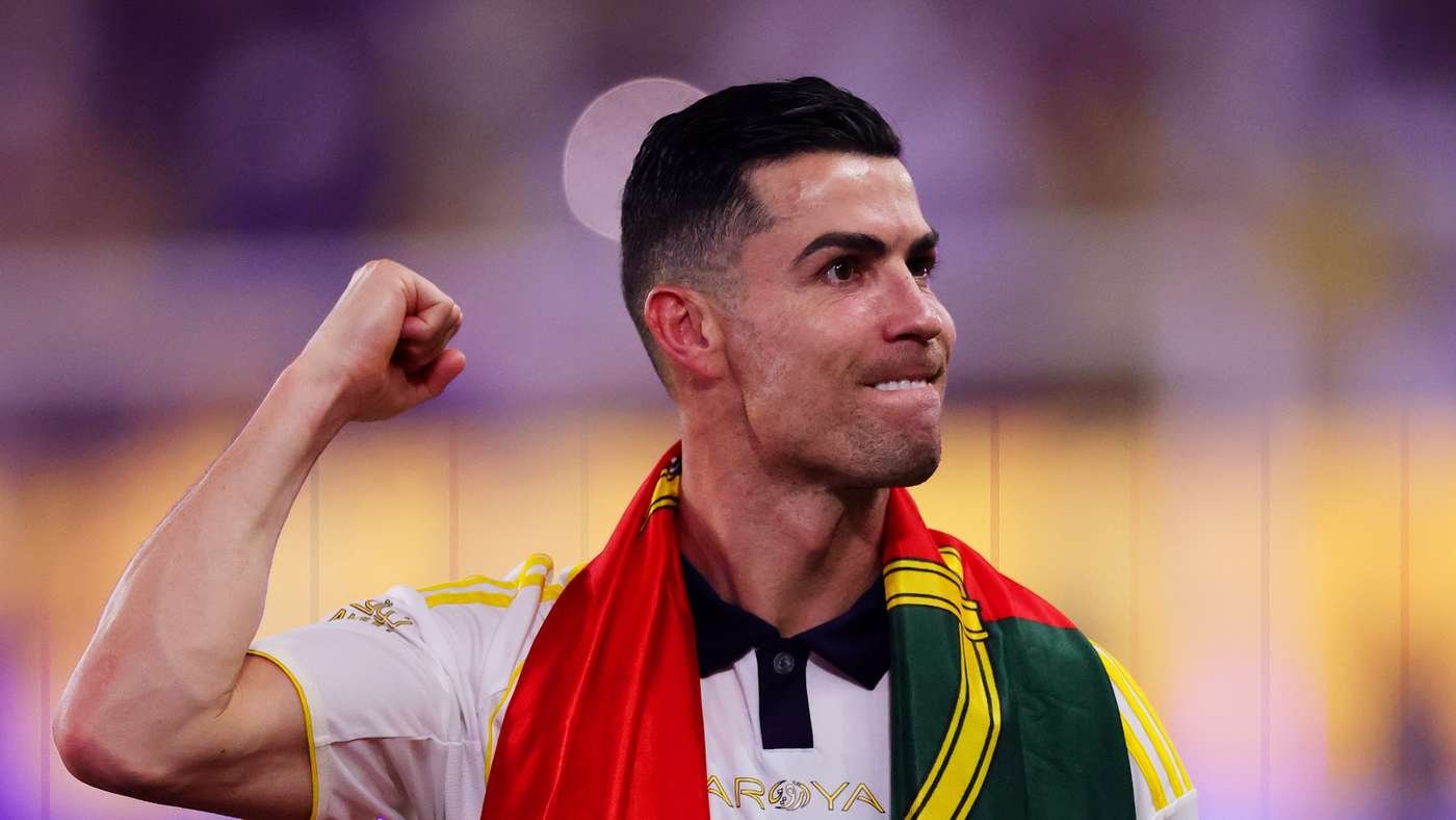 Soccer player celebrating with a Portuguese flag draped over shoulders, fist raised in a stadium.