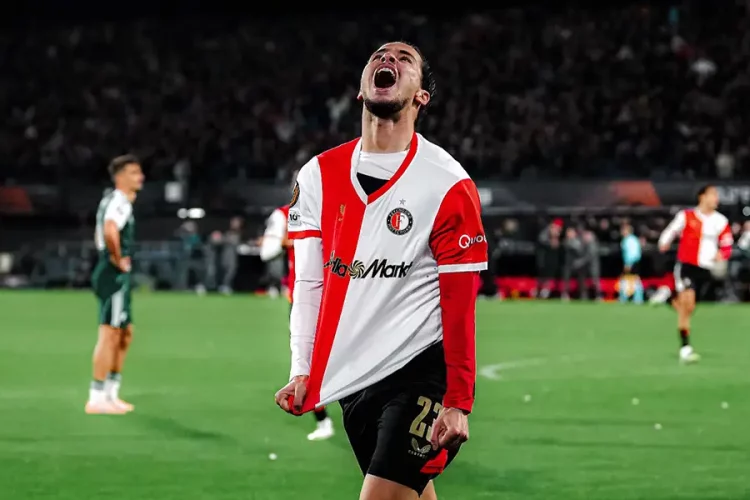 Soccer player in a white and red jersey celebrating with head tilted back and mouth open on a green field.