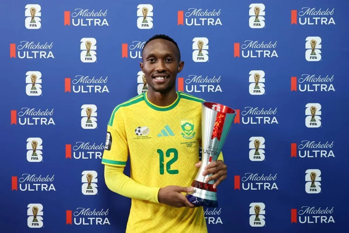 Soccer player in yellow jersey with number 12, holding a tall trophy in front of a blue backdrop with Michelob Ultra and FIFA logos.