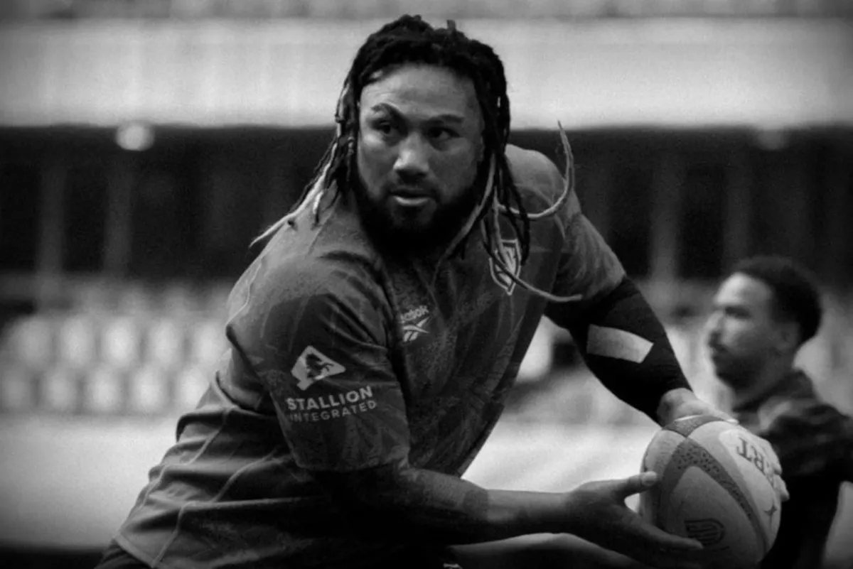 Rugby player with dreadlocks in action, gripping a rugby ball and looking ahead on the field.