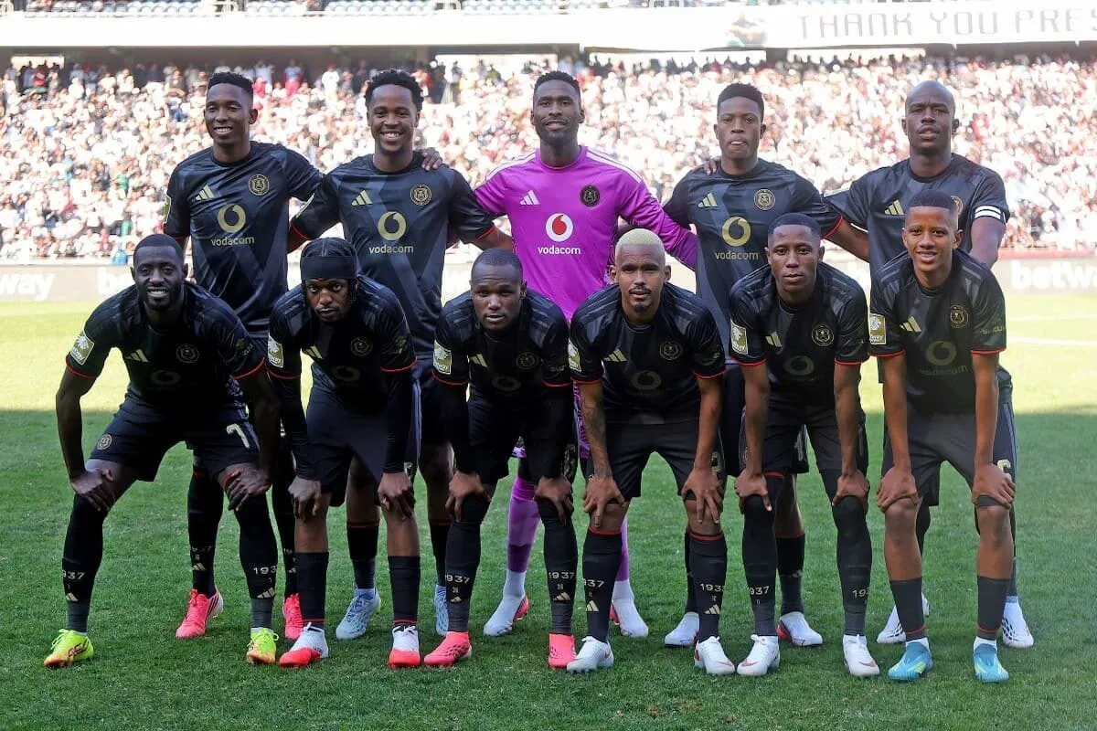 Football team posing for a group photo on the pitch, with a purple-clad goalkeeper in the center.