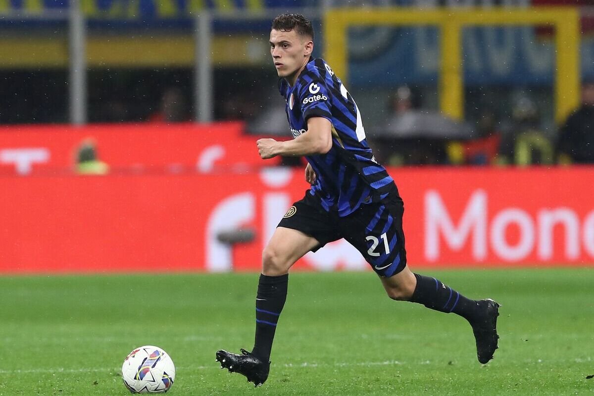 Footballer in a blue-and-black striped kit dribbles the ball on a green pitch during a match, sprinting forward.