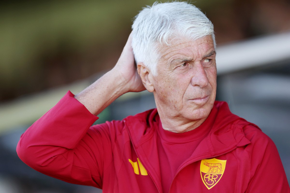 Older man with white hair in a red sports jacket looks to the right, hand behind his head.