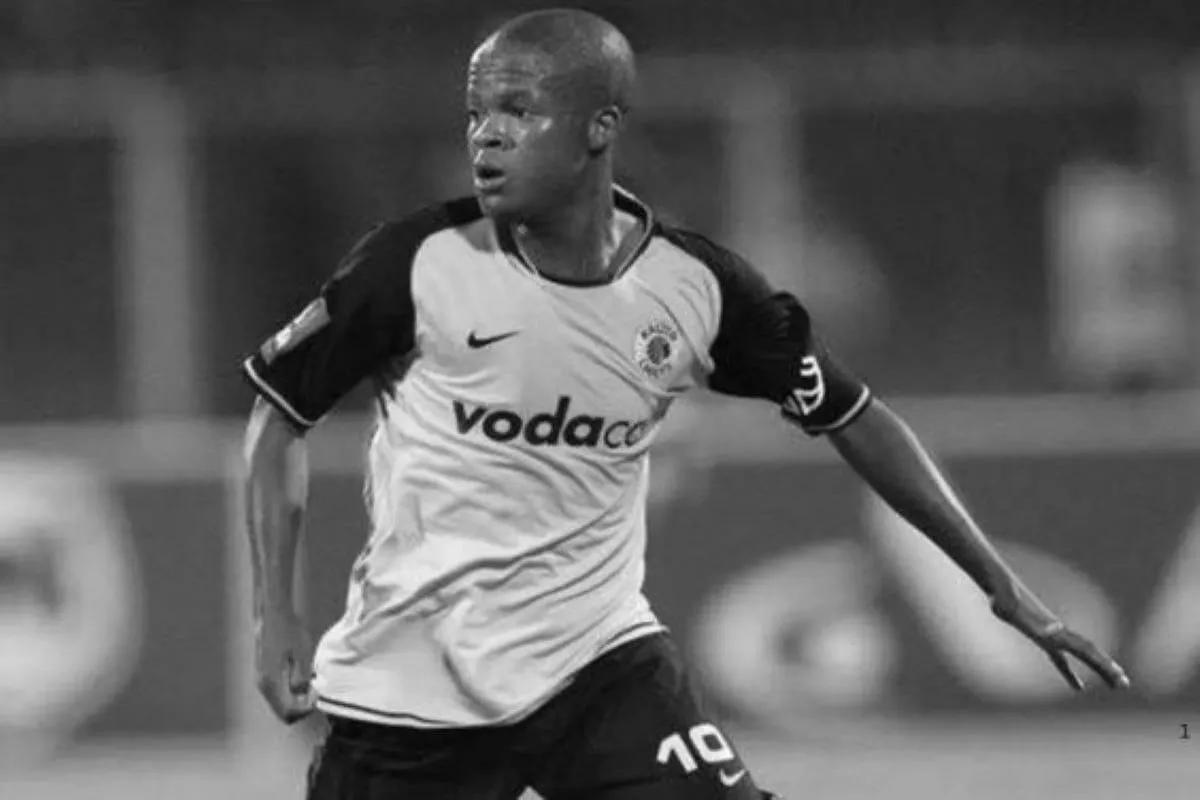 Black-and-white photo of a male soccer player in a white jersey with vodacom sponsor, sprinting on the pitch.