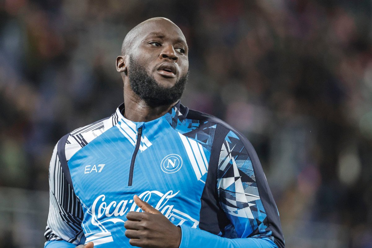 Professional footballer in a blue Napoli training jersey, running on the field with a determined expression.